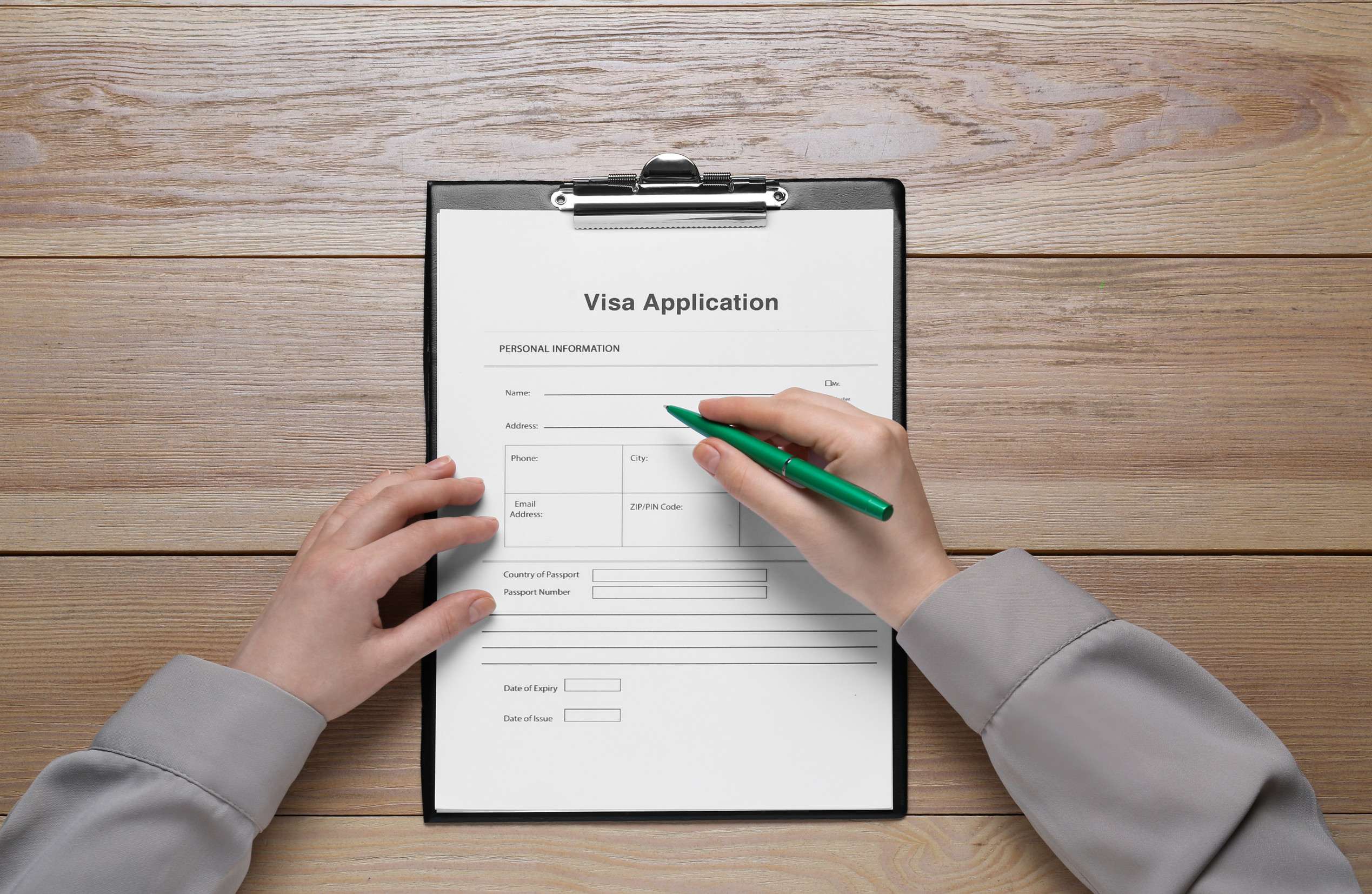 Woman Filling Visa Application Form On Wooden Table Top View